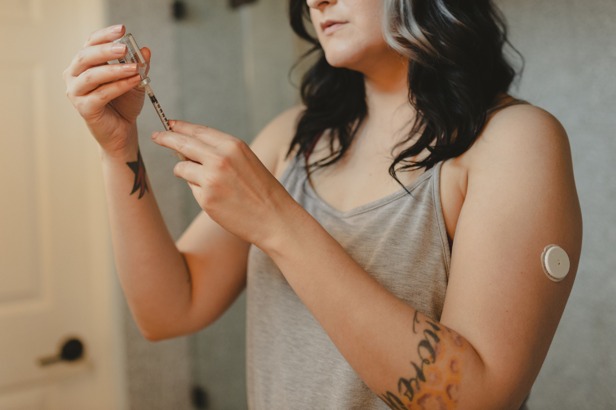 Woman wearing vest top, tattoos, with needle and insulin 