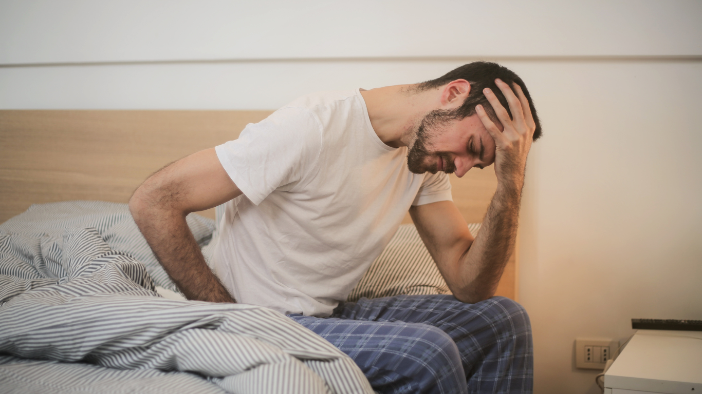 Younger male sat on bed in pyjamas with his head in hand