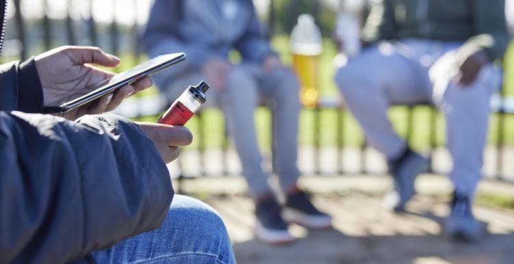 three teens in park, one is holding a vape in their hand