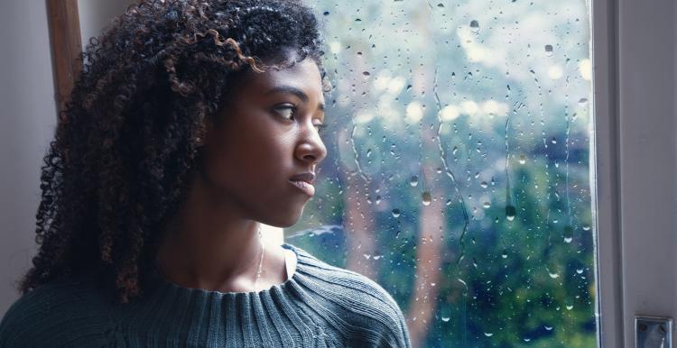 Young woman stood next to a window looking out at the rain