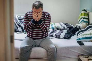 Man sat on edge of bed holding hands over face