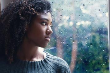 Young woman stood next to a window looking out at the rain